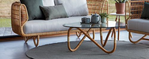 A stylish seating area featuring a woven sofa, a glass-top coffee table, and decorative pillows on a textured rug.