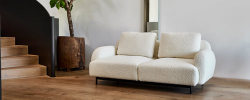 Cozy, modern two-seater sofa with soft cushions on a sleek metal frame, accompanied by a stylish planter and minimalist decor.