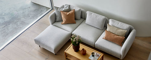 A stylish light gray sofa with cozy pillows, complemented by a wooden coffee table and a small potted plant.