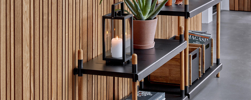 Stylish shelving unit with a lantern, potted plant, and decorative storage boxes, all against a wooden backdrop.