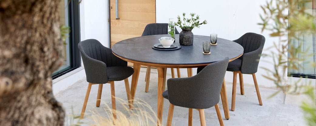 A round table with wooden legs surrounded by four stylish black chairs, adorned with a vase of flowers and glassware on the table.