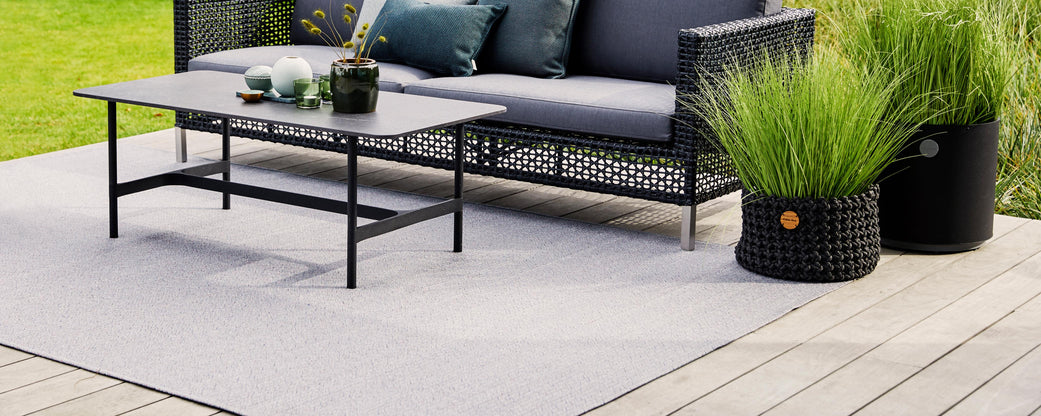 A stylish seating area featuring a black coffee table, a plush sofa with cushions, and decorative planters with tall grass.