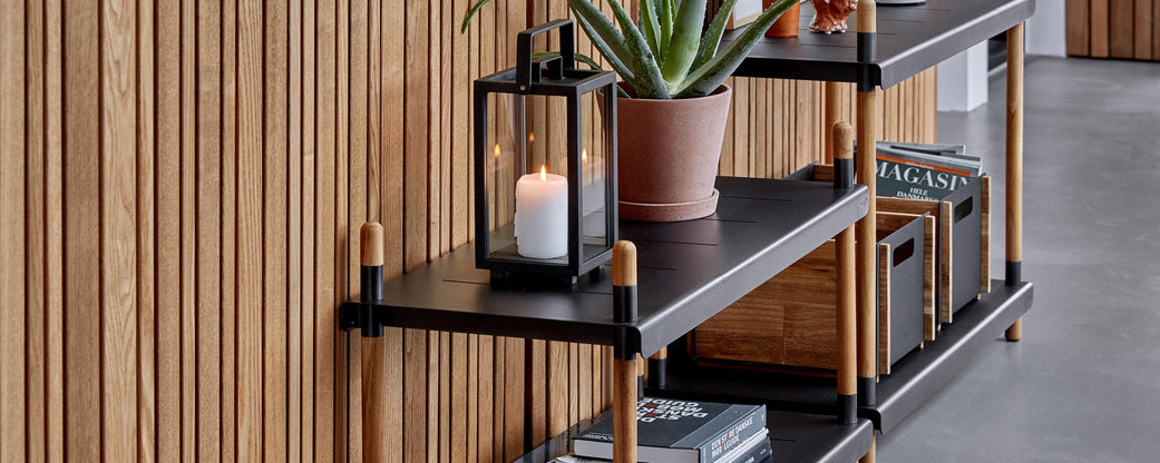 Stylish shelf unit featuring a plant, candle lantern, and storage boxes, complemented by a textured wooden backdrop.