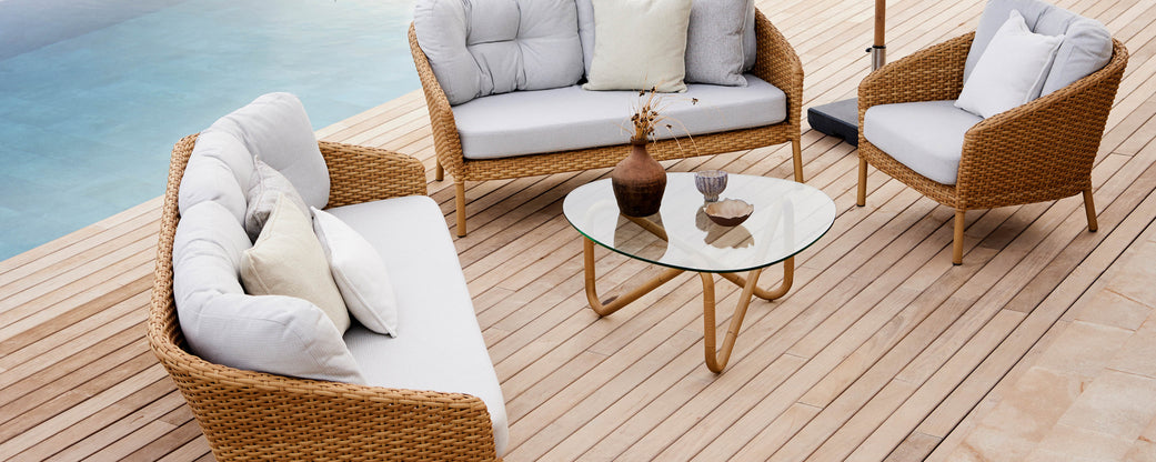 Stylish seating arrangement featuring a wicker sofa, chairs, and a glass coffee table, ideal for relaxing and entertaining.