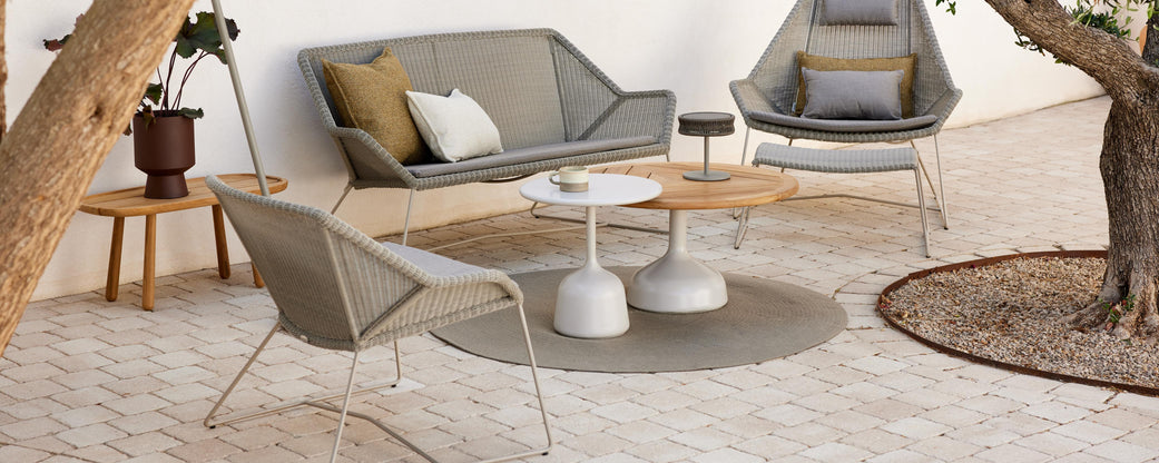 A modern seating arrangement featuring a sofa, chairs, and various side tables, surrounded by a natural setting.