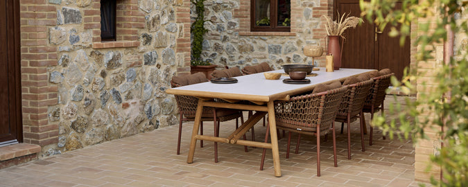A wooden dining table set with stylish wicker chairs, adorned with a decorative bowl and a minimalist table setup.