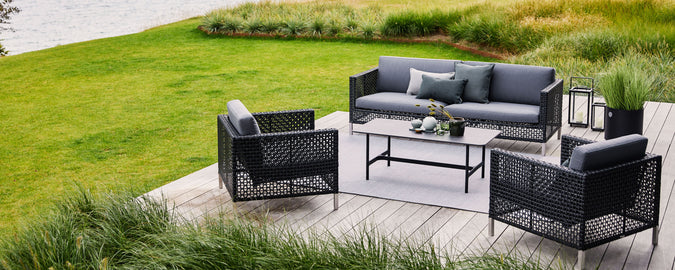 Stylish outdoor seating arrangement featuring a gray sofa and two armchairs with a coffee table, surrounded by lush greenery.