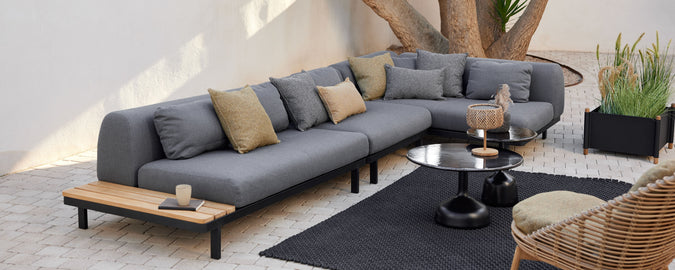 Lounge area featuring a modern sectional sofa with decorative cushions, a round coffee table, and a stylish rug, complemented by greenery.