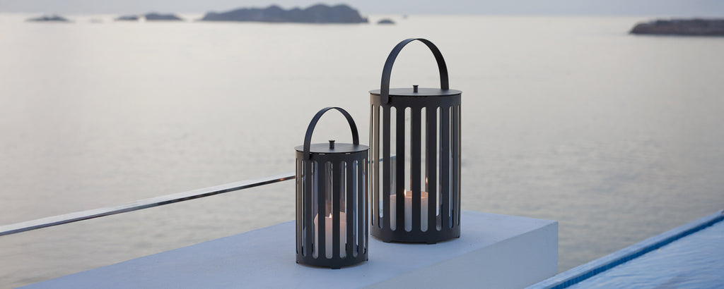 Two modern black lanterns on a surface overlooking a serene seascape.