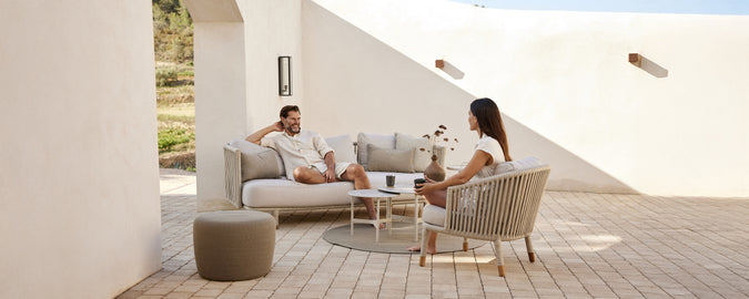Modern lounge area with beige sofa, white cushions, grey chair, and round table.