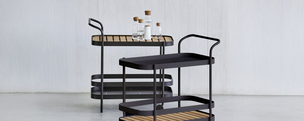 Modern black serving cart with brown tray in a stylish lounge setting.