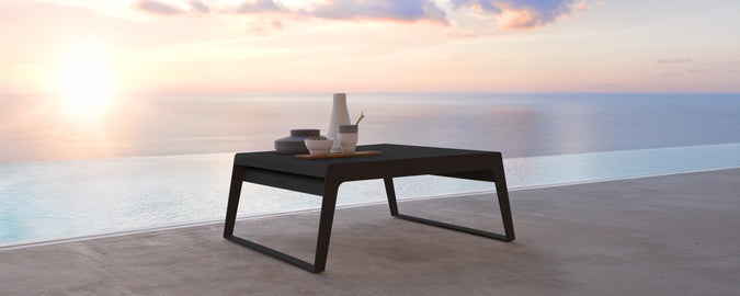 Modern black table on a terrace with a view of the sunset over water.