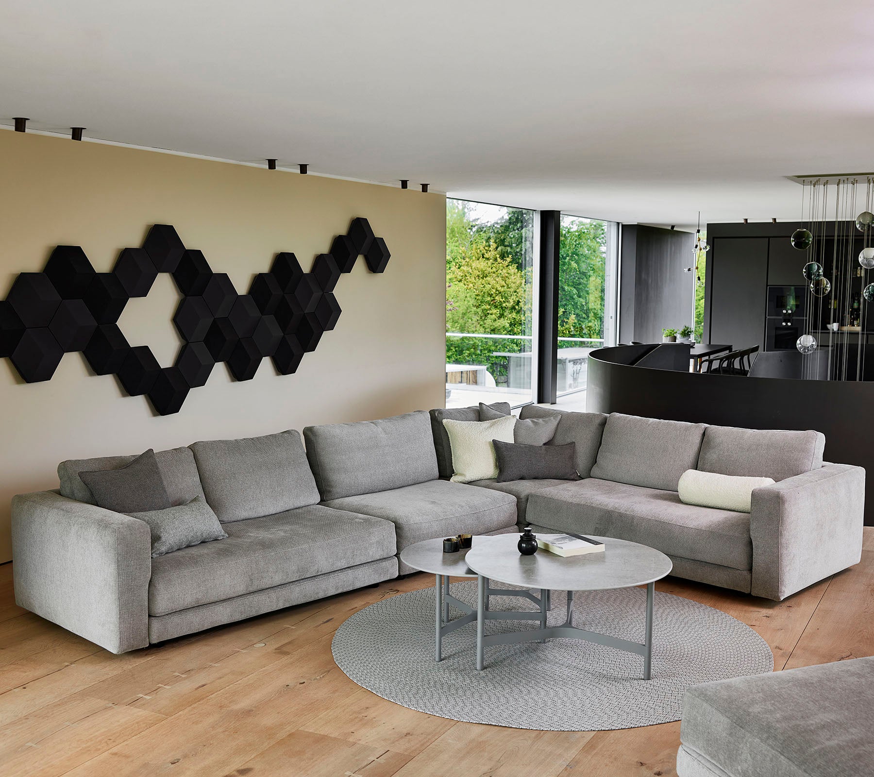 A modern gray sectional sofa with decorative cushions, a round coffee table, and a textured black wall art piece.