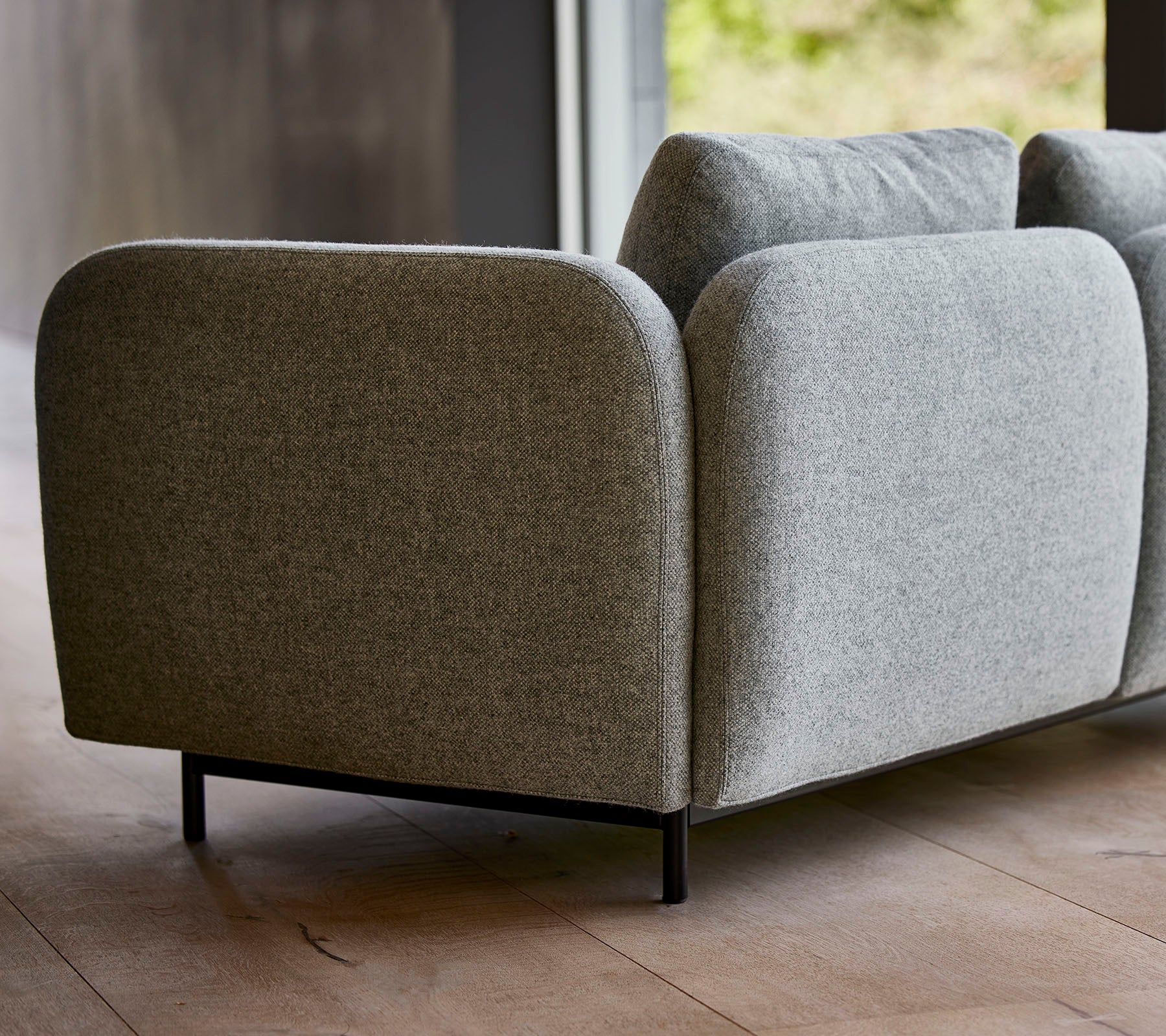 A modern grey upholstered sofa with rounded edges and sleek black legs, showcasing a minimalist design.