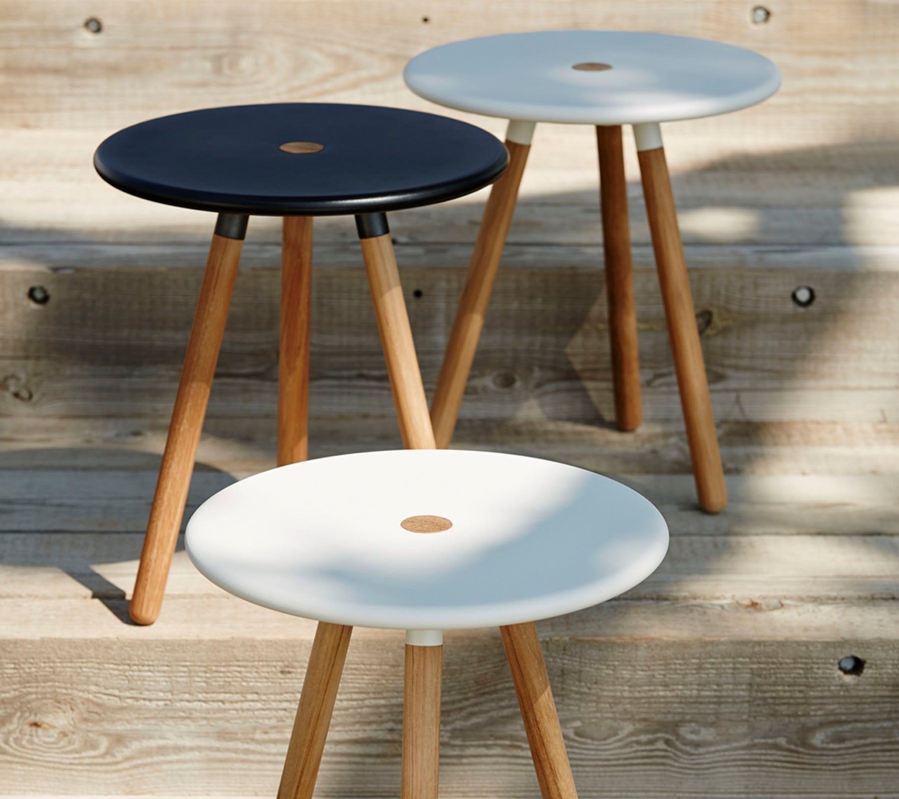 Three minimalist stools with round tops in black and white, each supported by wooden legs, showcasing a modern and stylish design.
