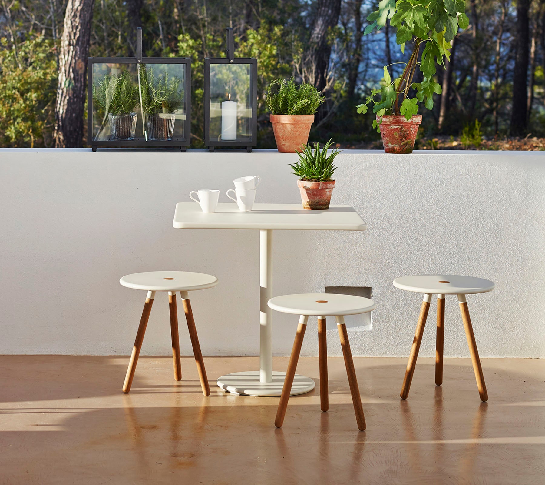 A minimalist table with three matching stools, surrounded by potted plants, creating a serene and inviting atmosphere.