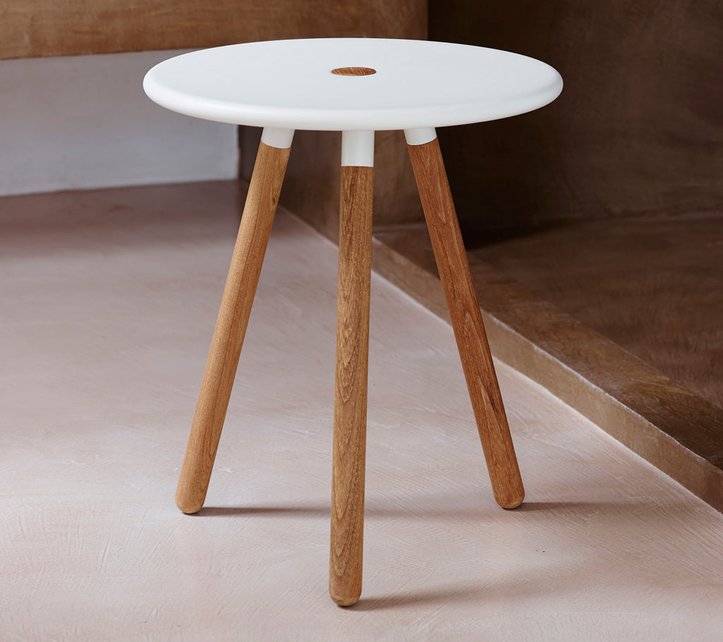 A modern round table with a white top and natural wooden legs, featuring a small hole in the center for design interest.