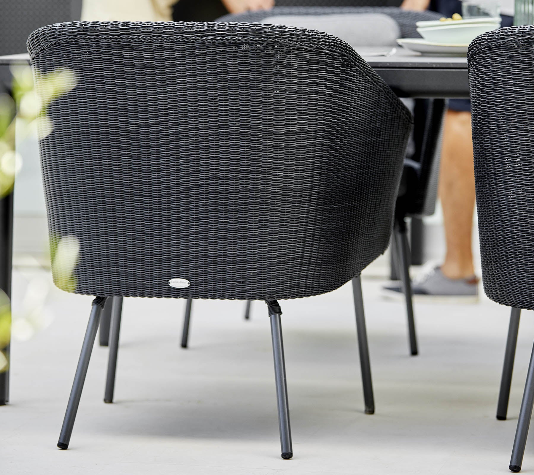 Black woven chair with curved backrest and metal legs, positioned near a dining table with soft focus on surrounding elements.