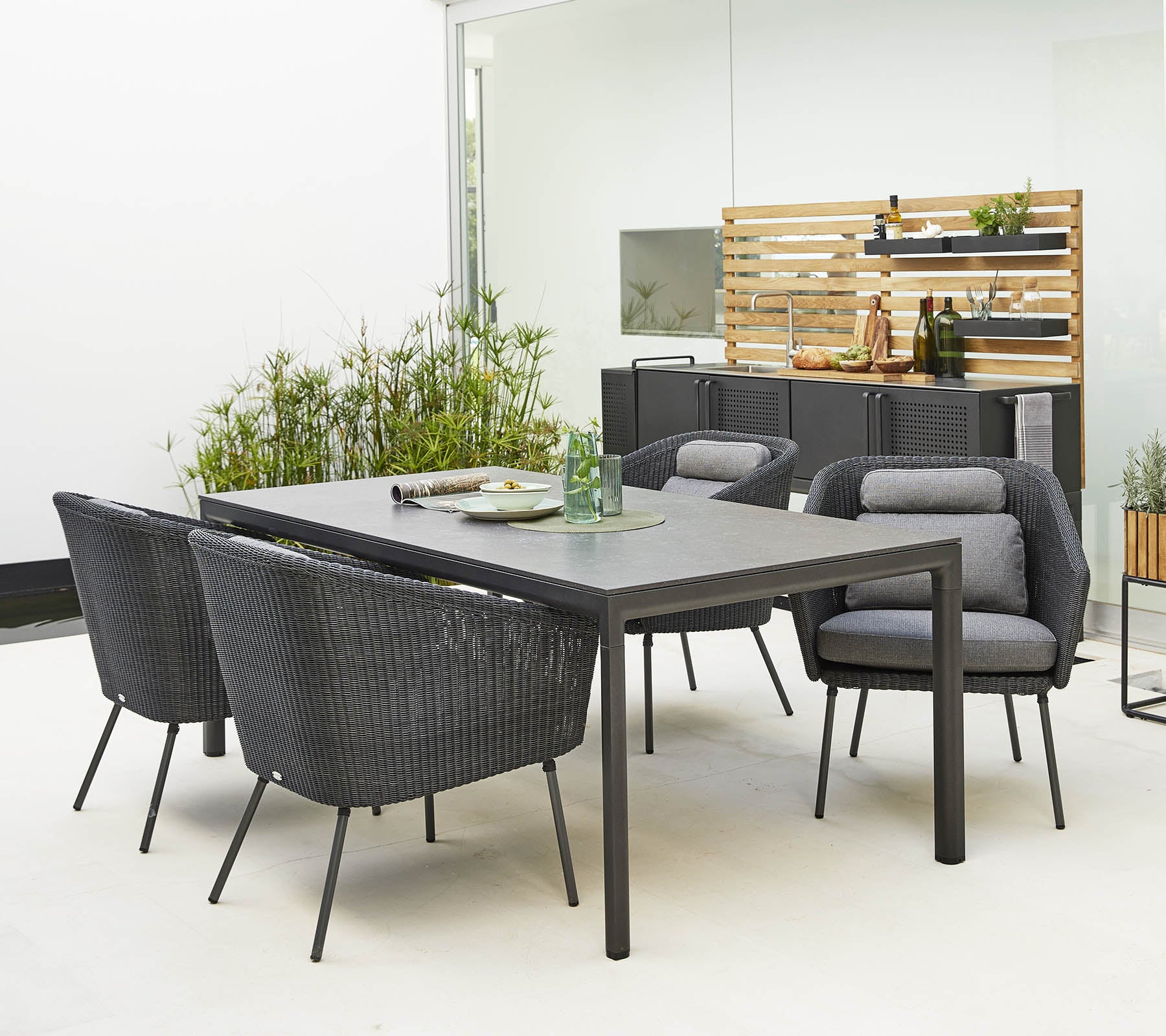Stylish outdoor dining set featuring a sleek table and comfortable, modern chairs surrounded by decorative greenery.