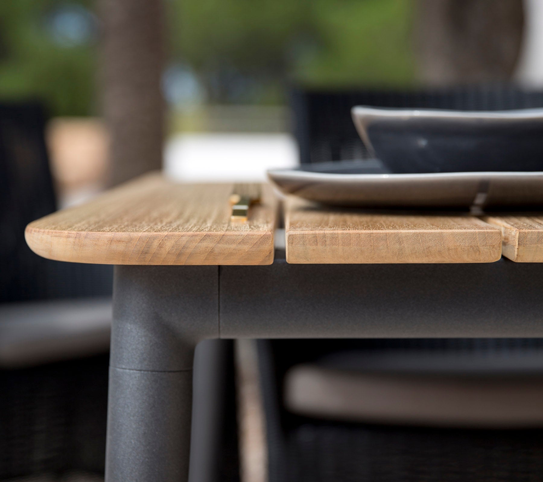 Close-up of a wooden table edge featuring a smooth finish, with a black plate placed on top, showcasing a modern design.