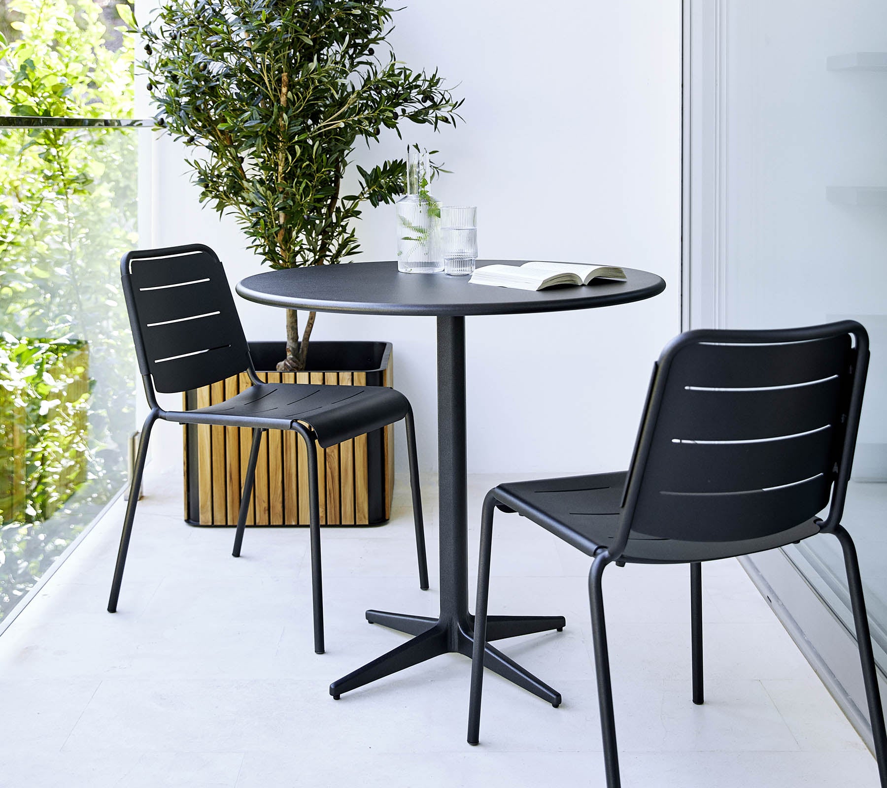 Small round table with two black chairs and a potted plant nearby, creating a minimalist and stylish setting.