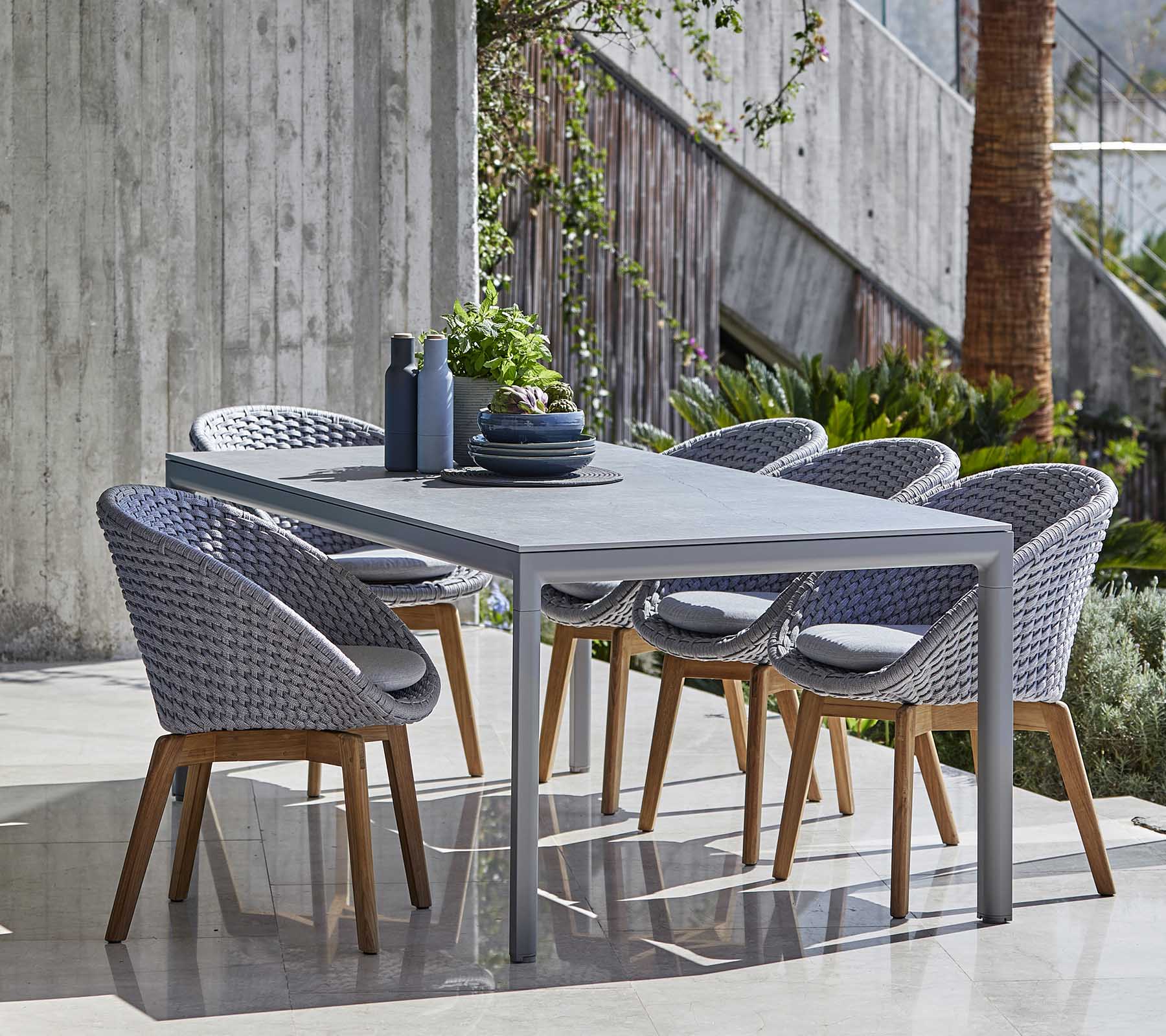 Modern dining set featuring a grey table and woven chairs with wooden legs, arranged neatly with decorative items on the table.