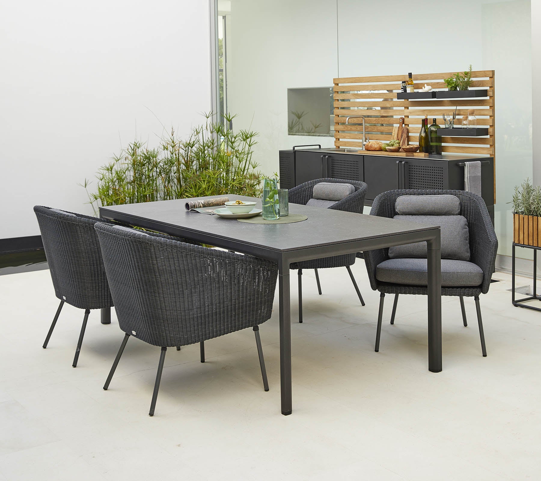 Modern outdoor dining set featuring a sleek table and four stylish chairs with comfortable cushions, surrounded by greenery.