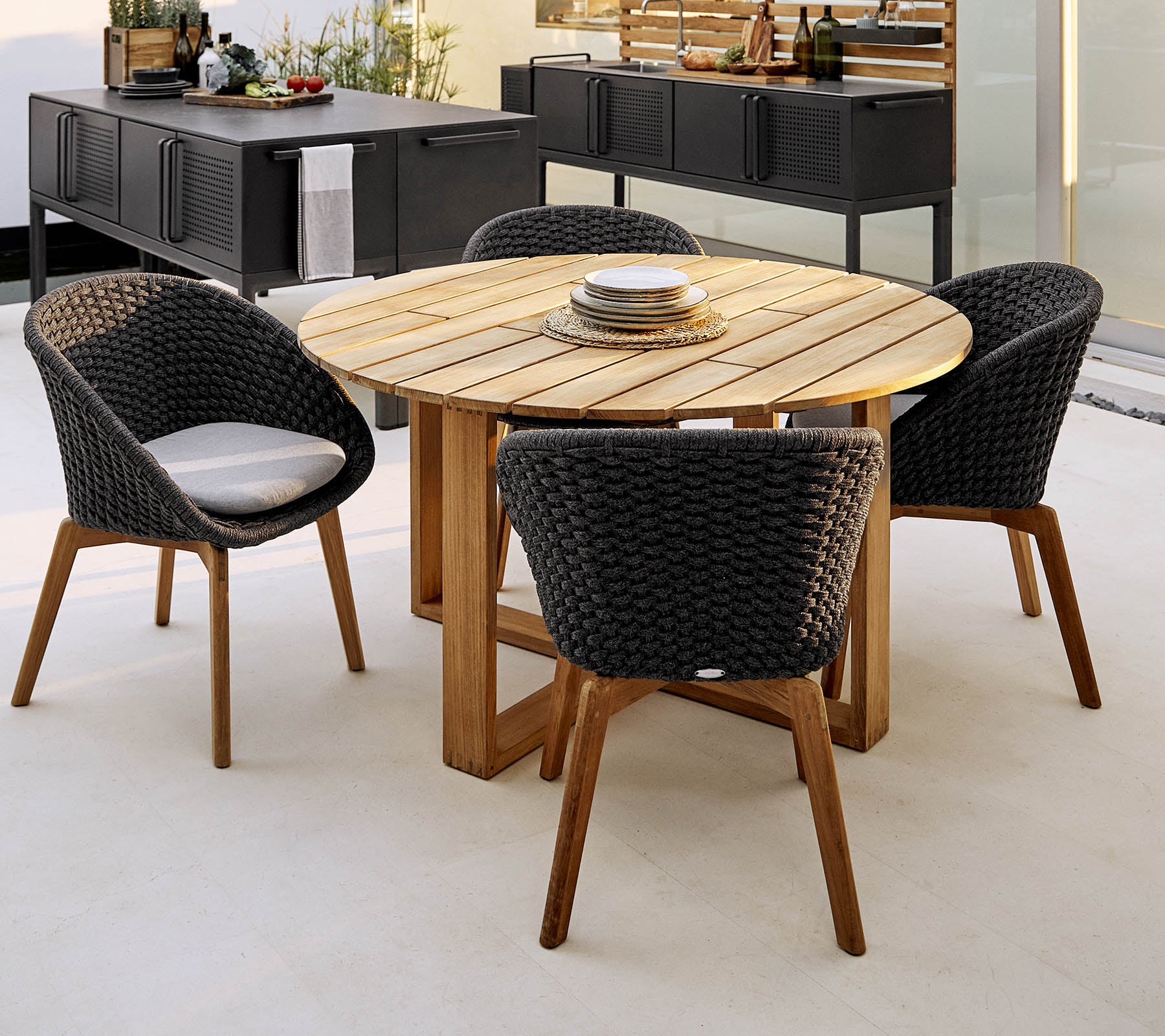 Round wooden table with four stylish woven chairs, perfect for dining and social gatherings. Elegant and inviting outdoor seating arrangement.