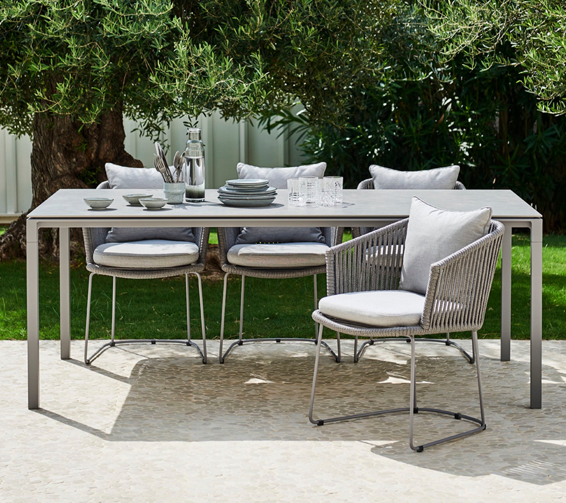 A modern outdoor dining set featuring a sleek table, cushioned chairs, and elegant dishware arranged for a stylish meal.