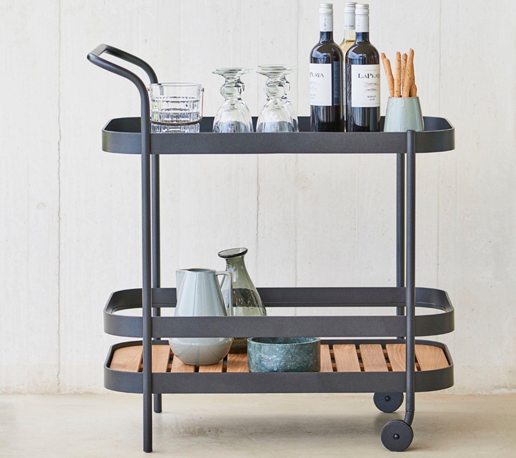 A stylish beverage cart featuring glassware, wine bottles, and utensils on three levels, with a sleek metal frame and wooden accents.