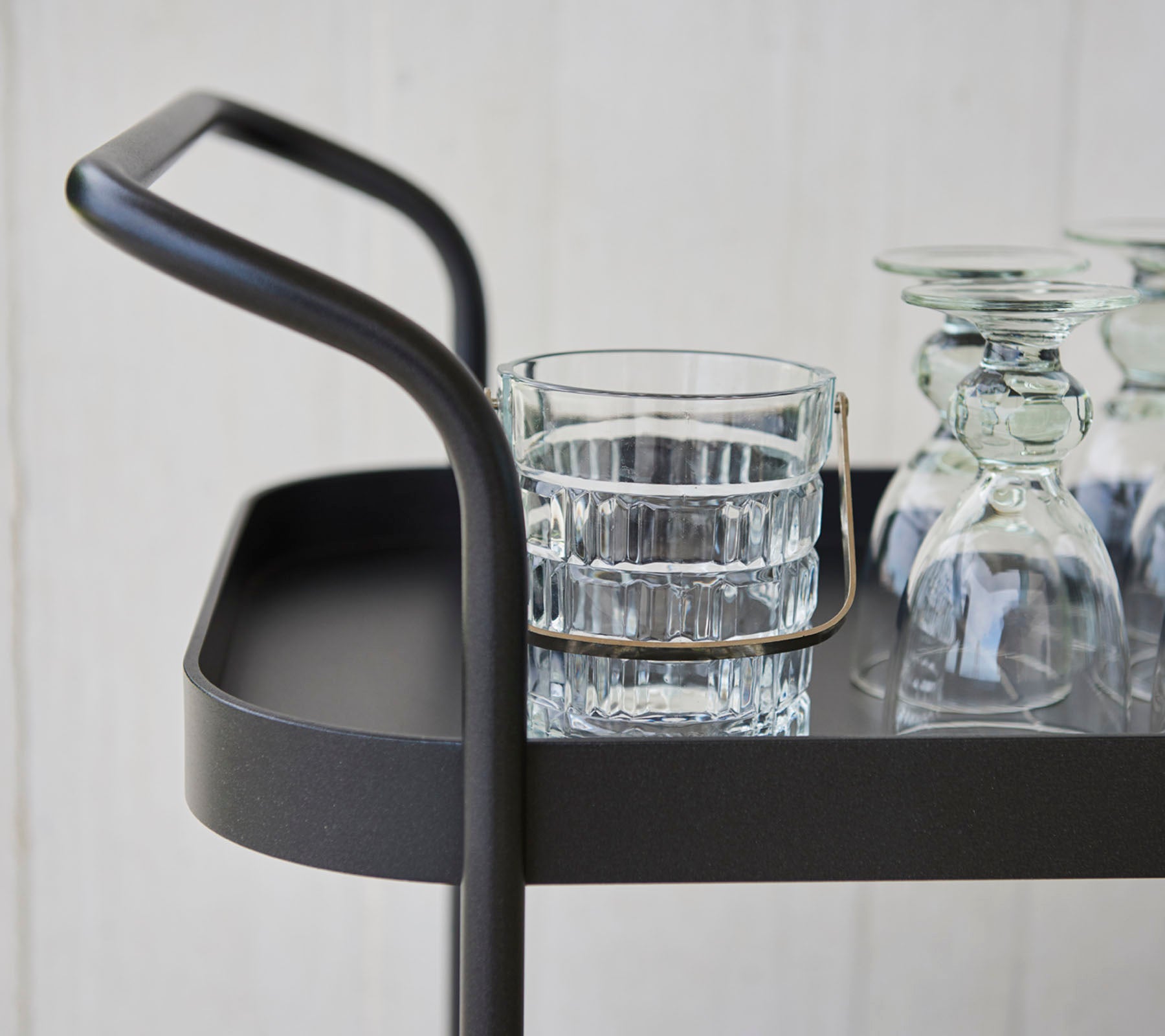 Stylish serving cart with a sleek handle, featuring a glass tumbler and several clear glassware pieces on a flat surface.