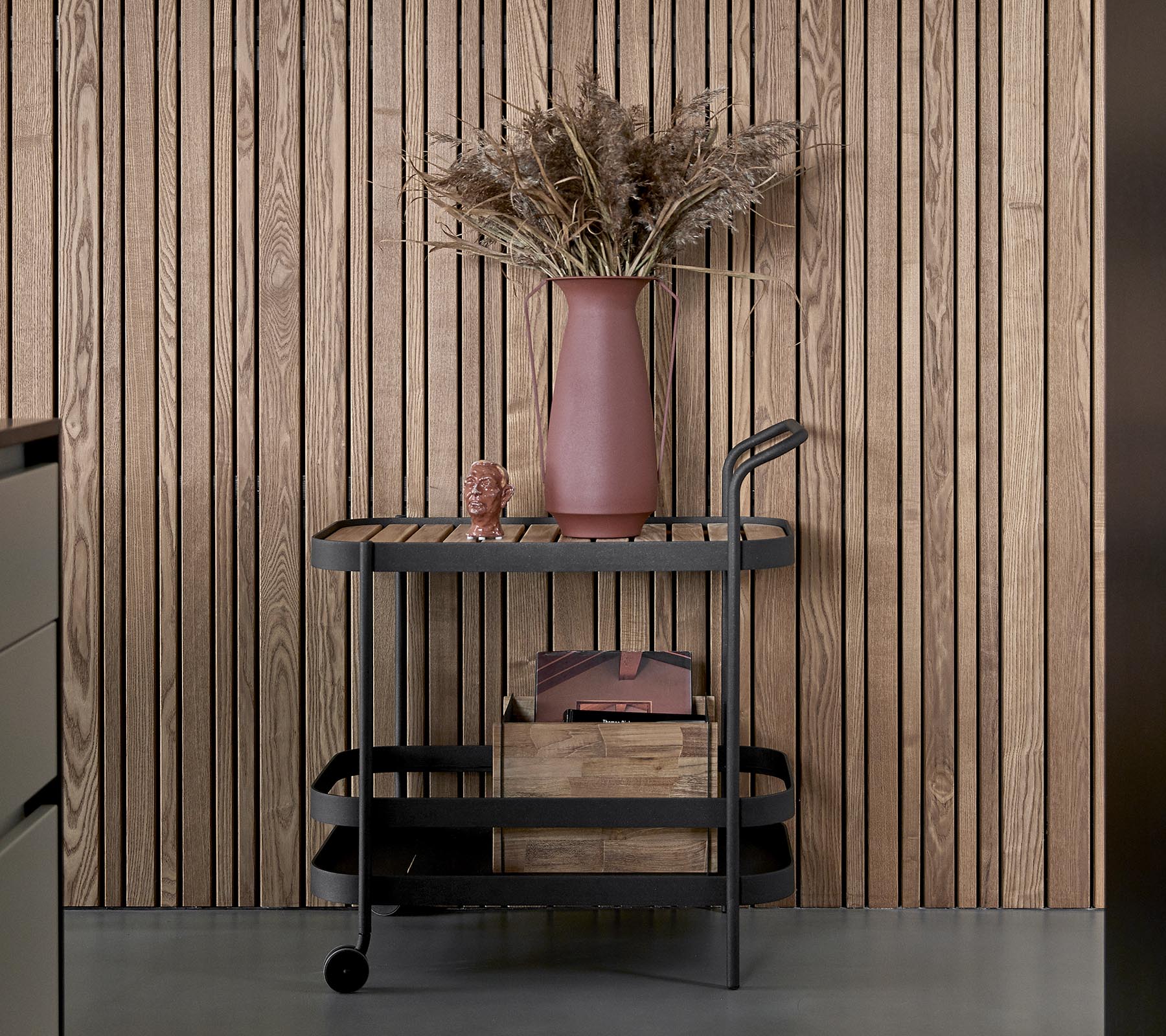 A sleek cart with a dark finish, featuring wooden storage boxes and a pink vase with dried flowers.