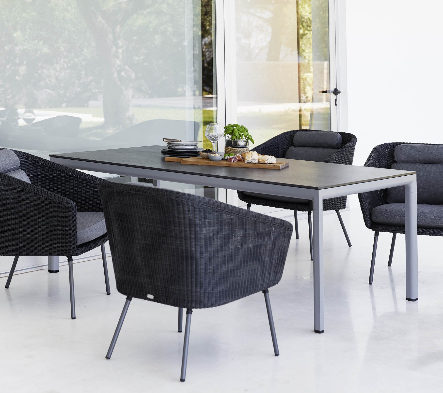 A modern dining table surrounded by four stylish black outdoor chairs, with a centerpiece and greenery on the table.