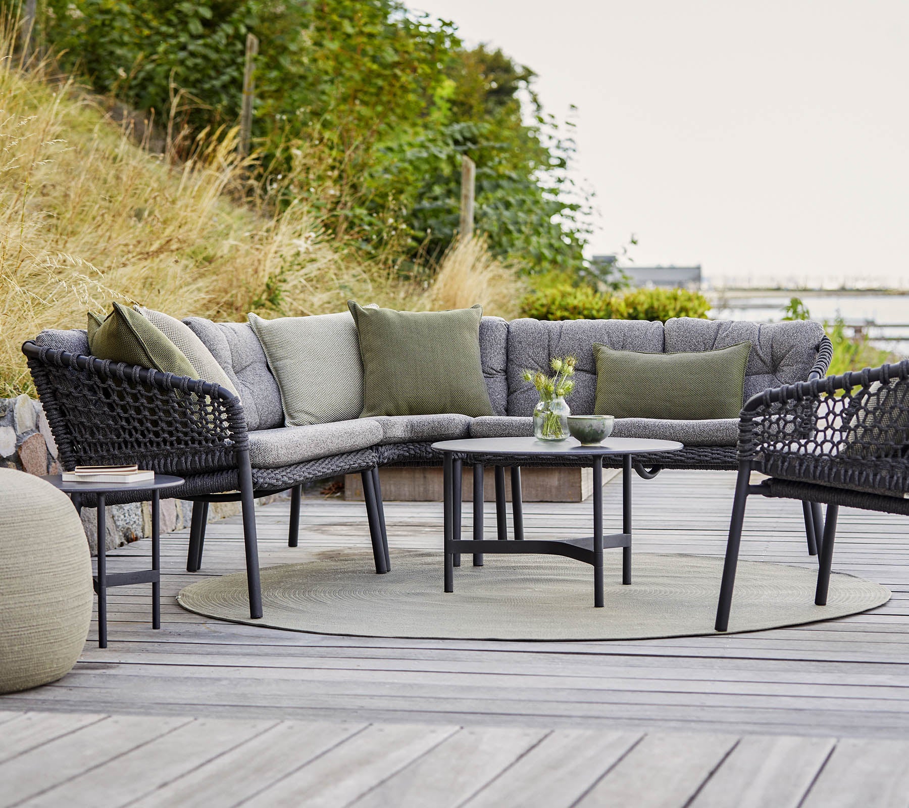 Stylish outdoor seating arrangement featuring a curved sectional sofa, round table, and cozy accents in a natural setting.