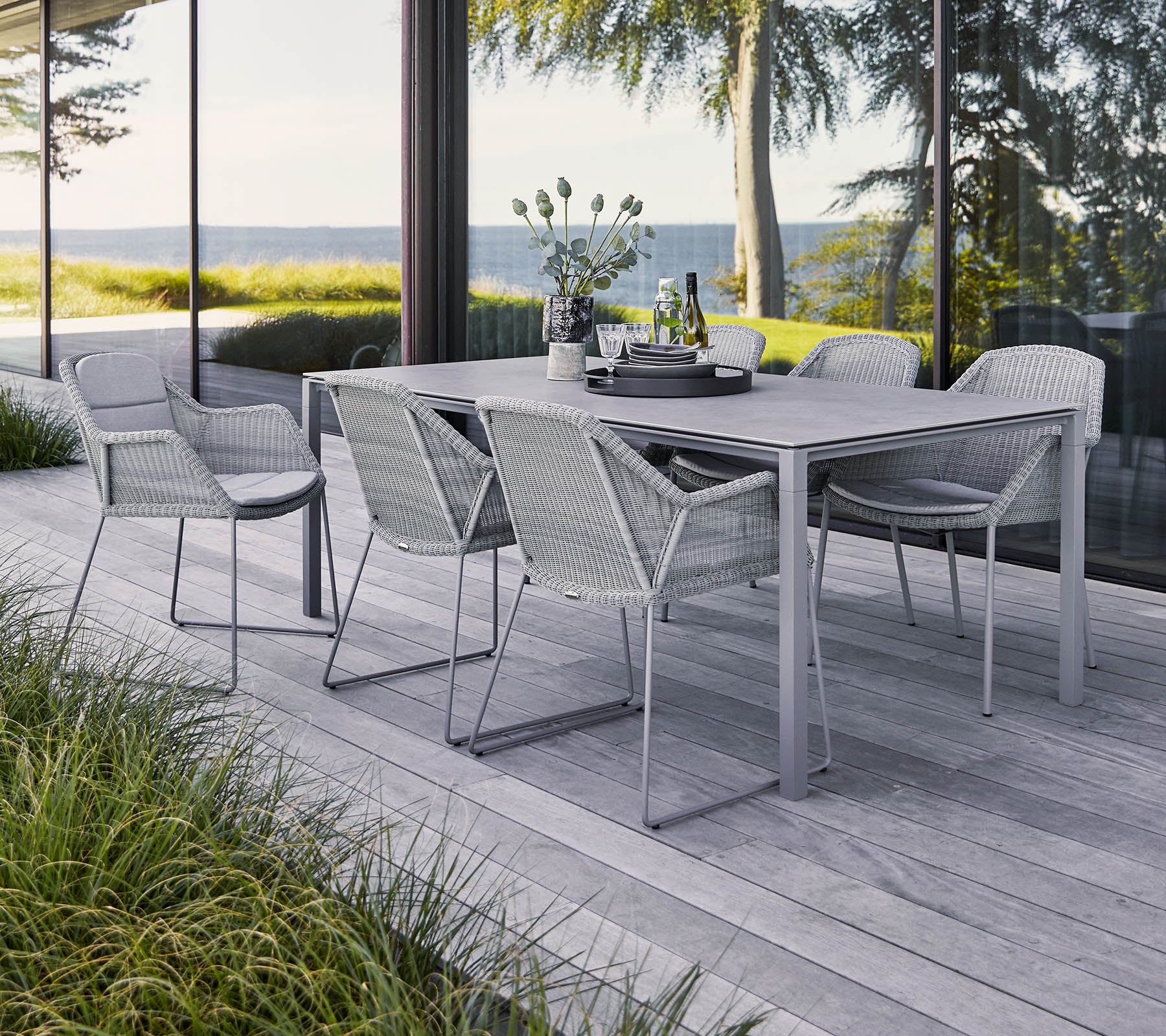 A stylish outdoor dining set featuring a rectangular table and six woven chairs, surrounded by greenery and a scenic view.