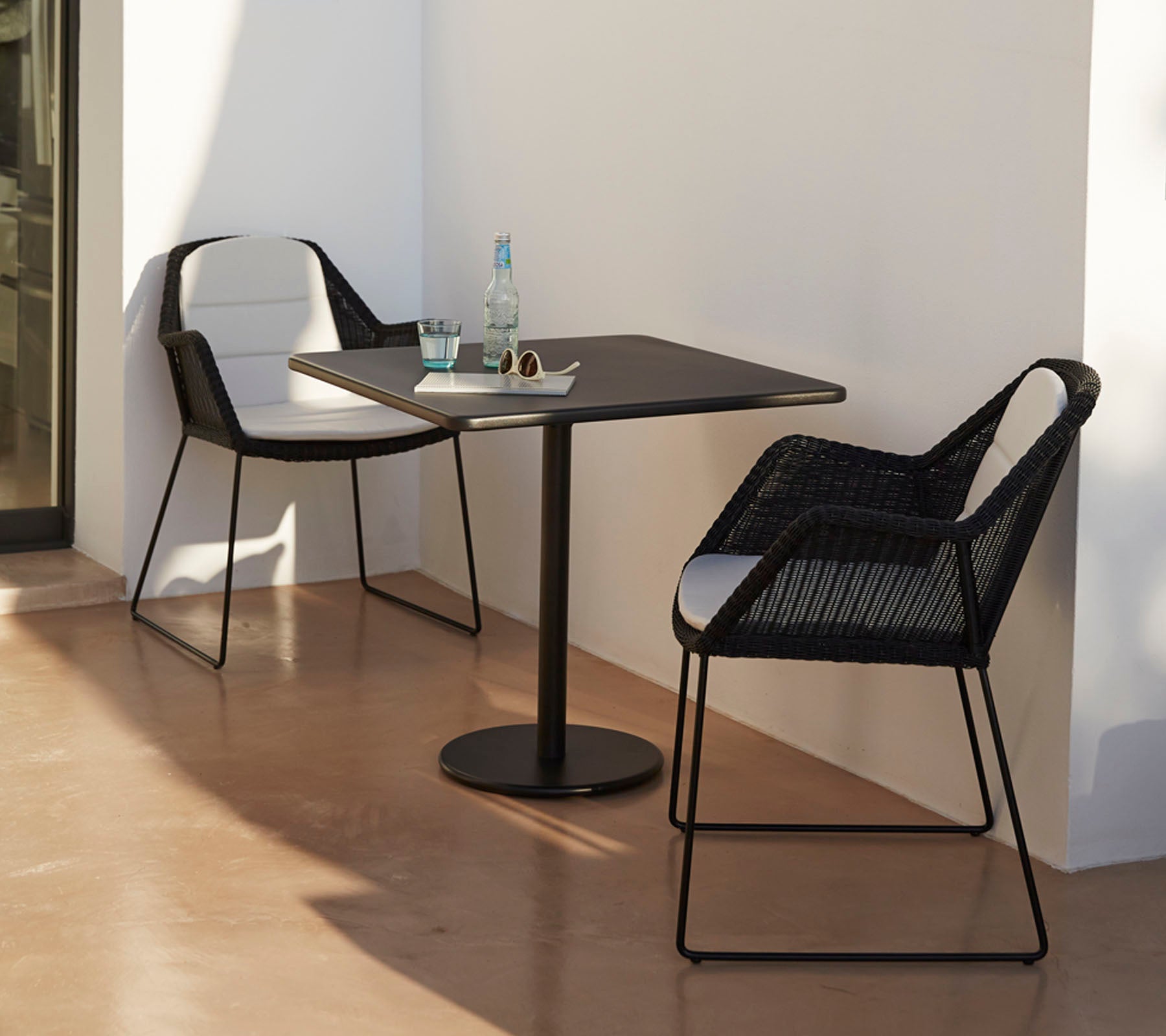 Modern table with two stylish black chairs, accompanied by a water bottle and sunglasses, set against a minimalist backdrop.