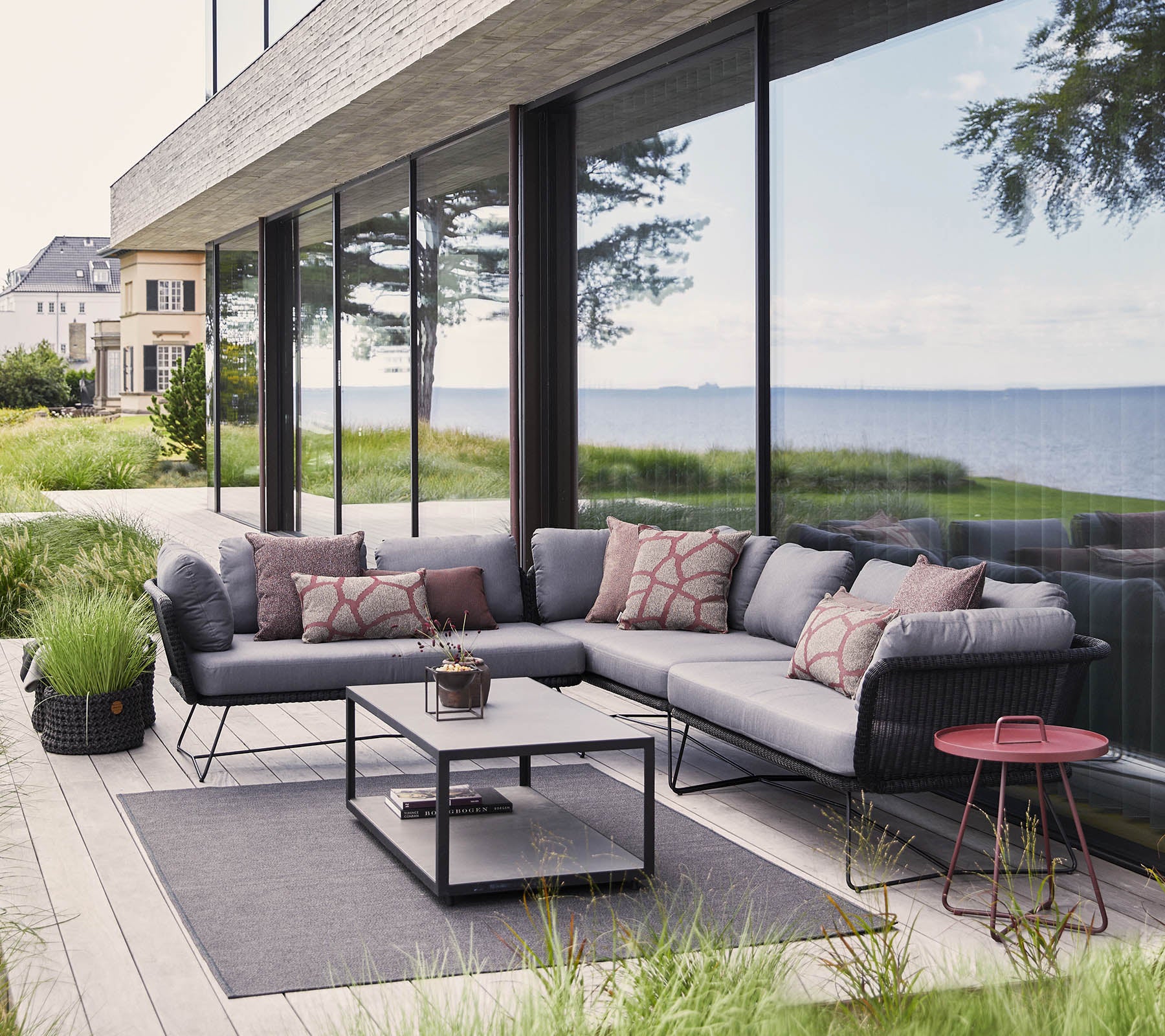 Modern outdoor seating area featuring a sectional sofa with cushions, a coffee table, and decorative elements amidst lush greenery.