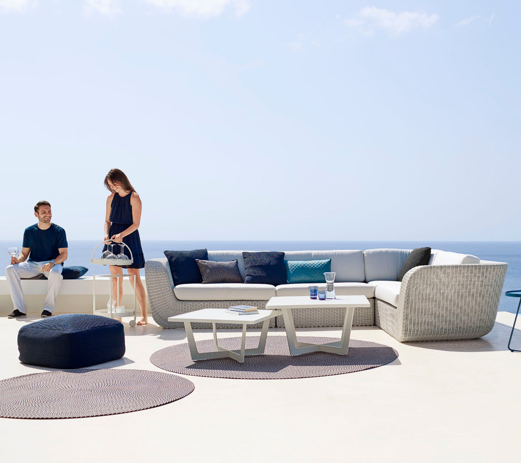 A modern outdoor seating area featuring a sectional sofa, coffee table, and decorative rugs, with two people enjoying the space.
