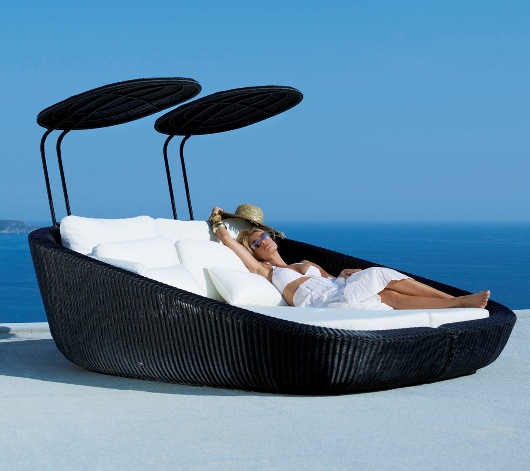A stylish outdoor lounge bed with a sleek design, featuring soft cushions and adjustable canopies, set against a scenic ocean backdrop.