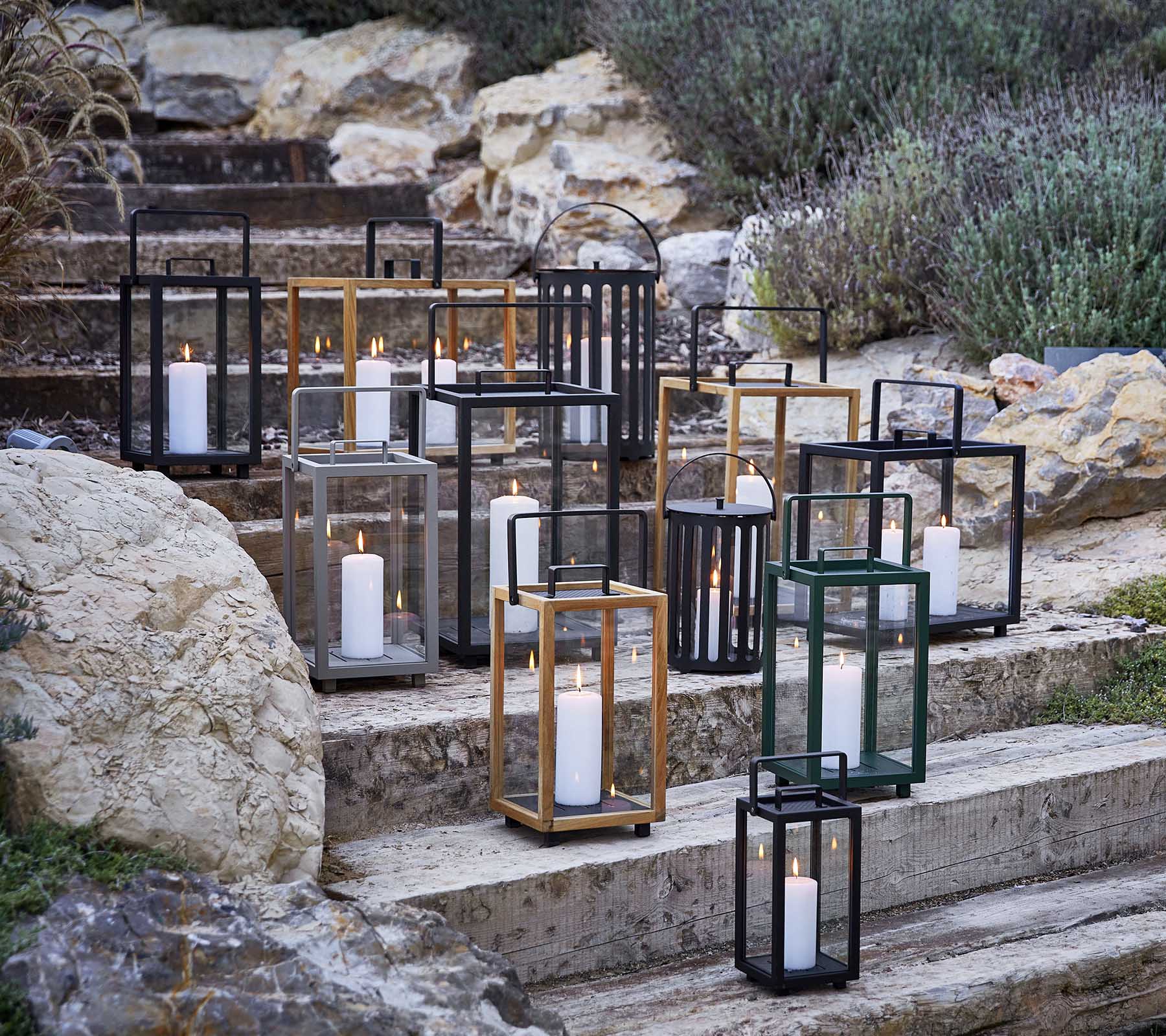 Collection of decorative lanterns in various styles and colors, featuring soft candlelight, arranged artistically on stone steps.