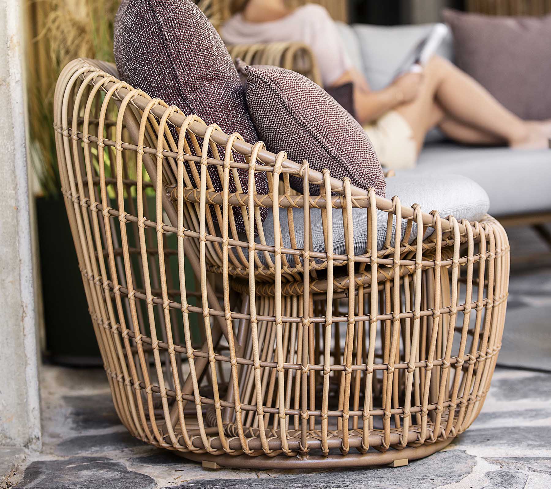 A stylish, woven chair with an open design, featuring two plush pillows for added comfort. Perfect for relaxed seating.