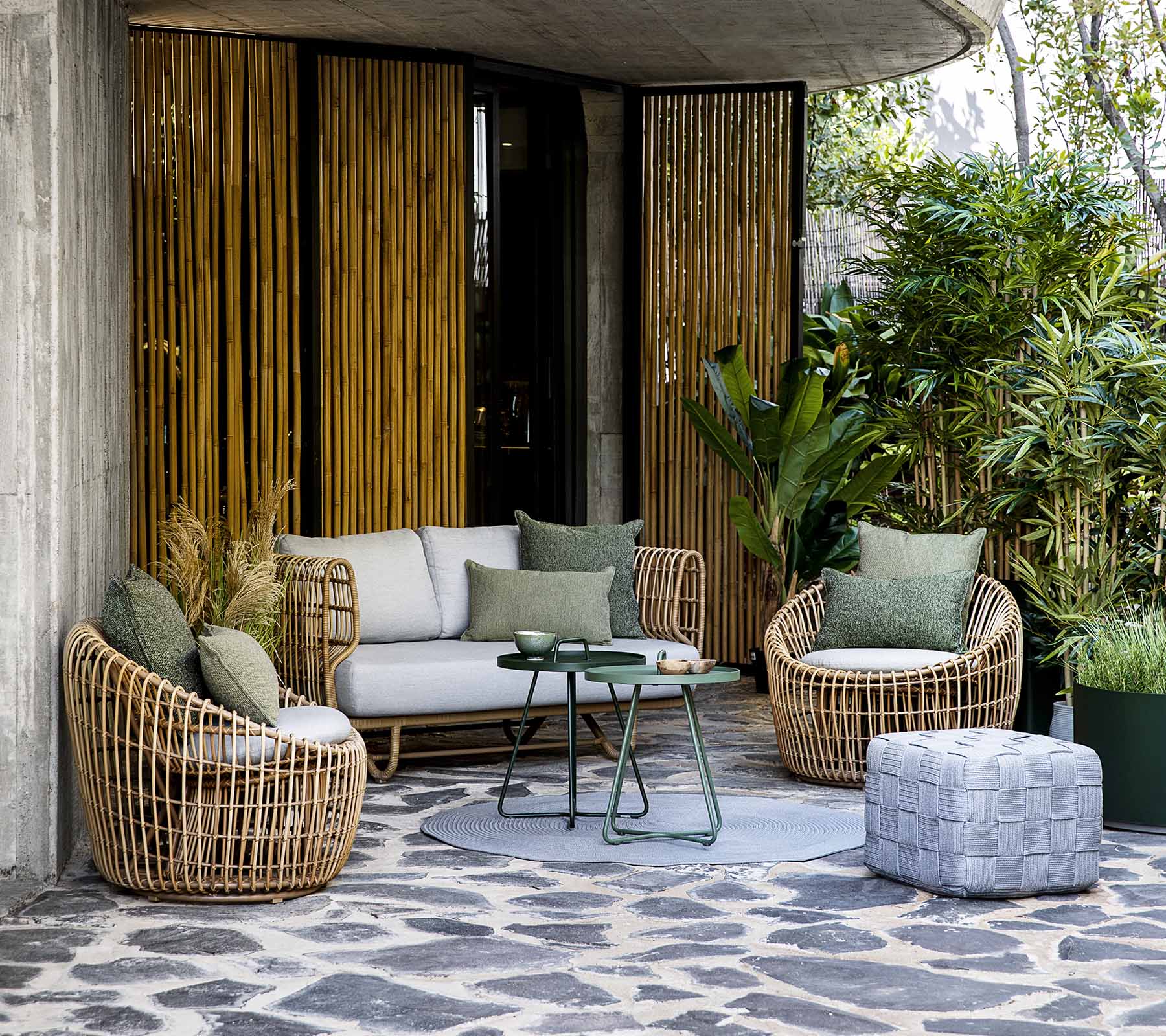Stylish seating area featuring a sofa and round chairs, complemented by cushions and a coffee table, surrounded by greenery.