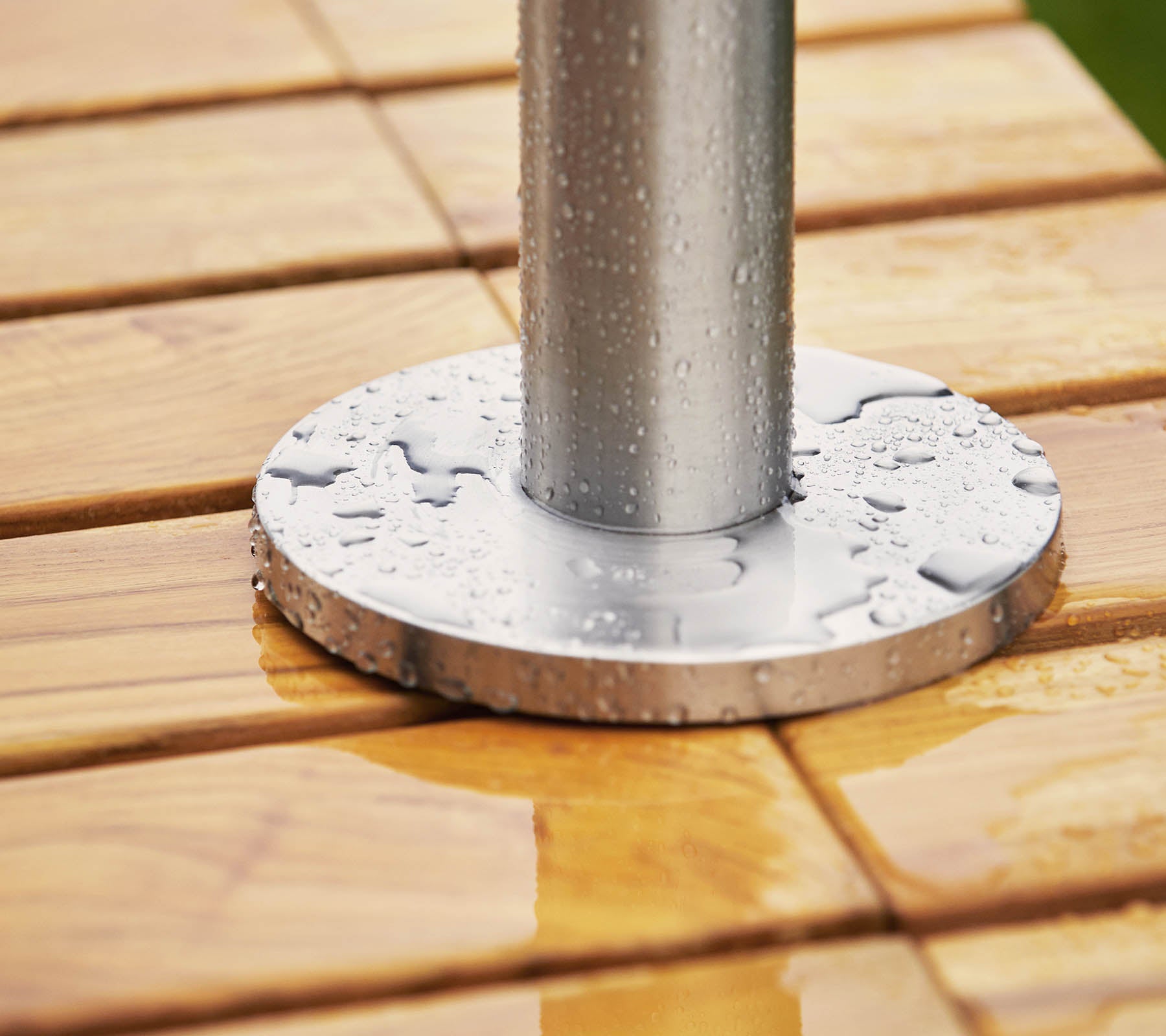 Metal base with a pole resting on a wooden surface, featuring water droplets on both the base and the wood.