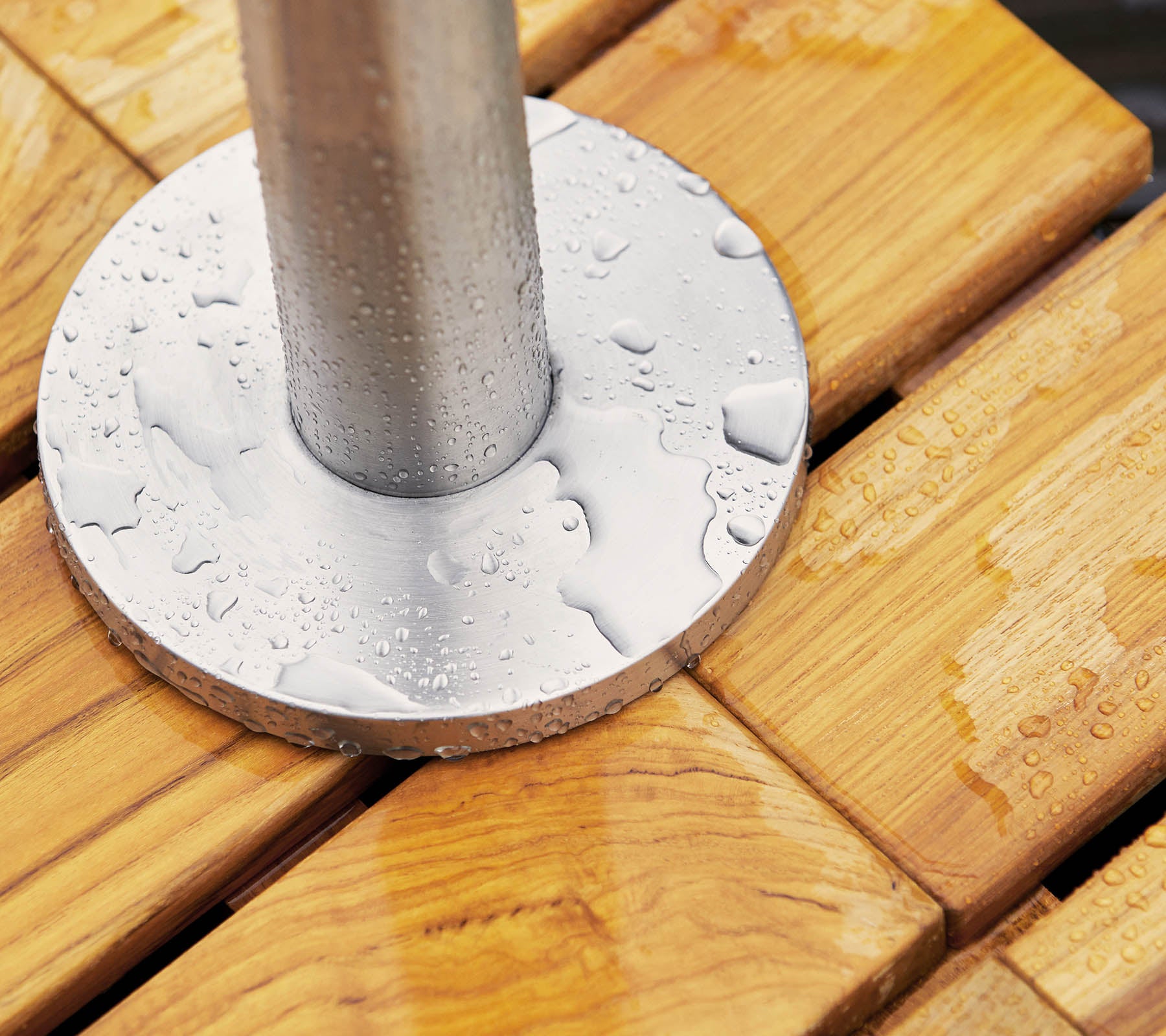 Metal base with water droplets resting on a wooden surface, featuring smooth, slatted planks and a cylindrical post at the center.