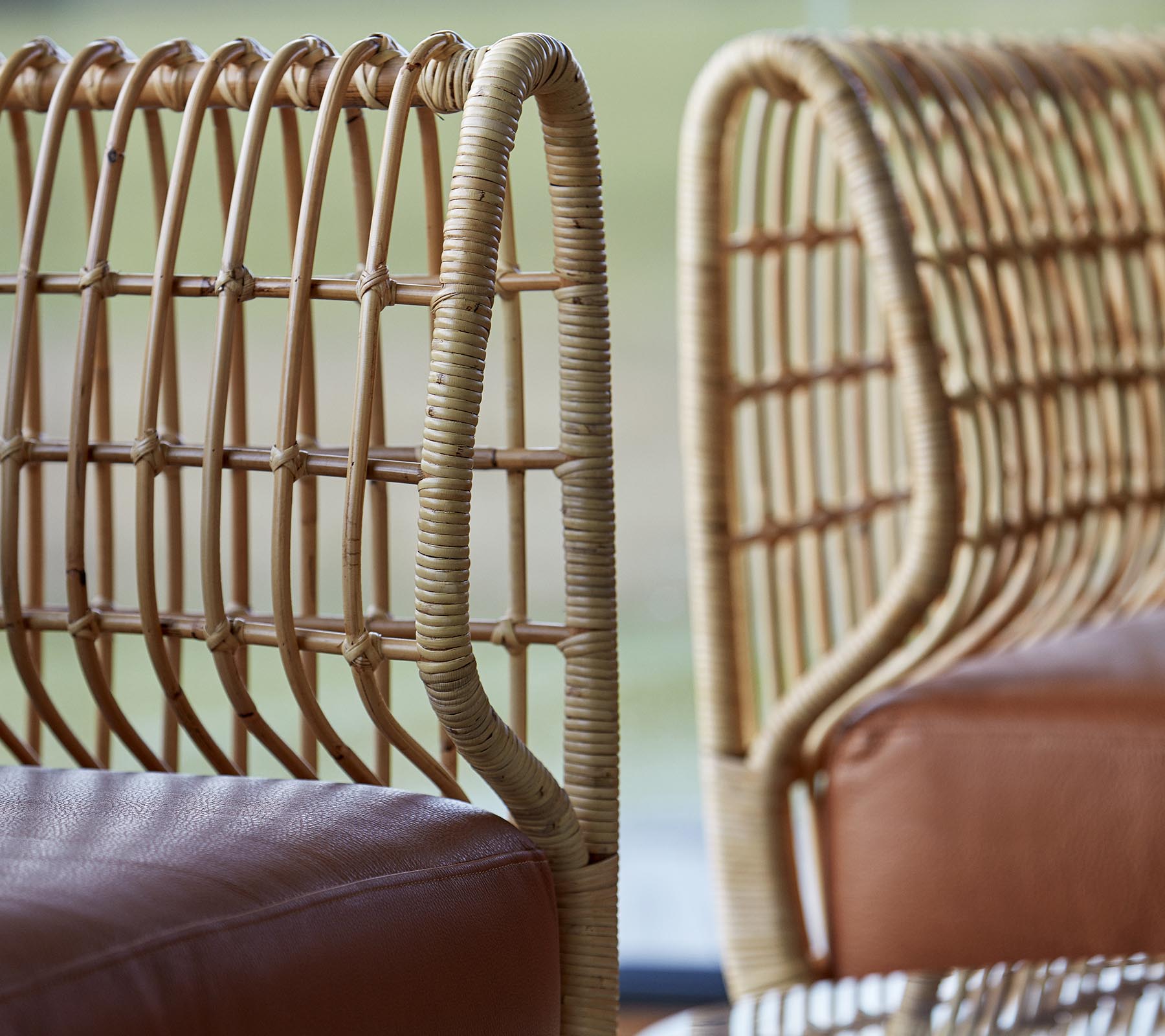 Two stylish chairs featuring woven rattan backs and smooth leather seats, showcasing a modern design aesthetic.