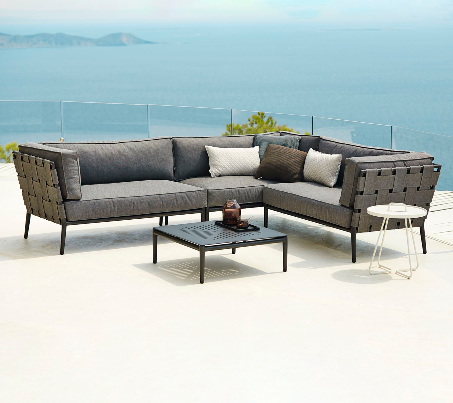 Modern outdoor seating arrangement featuring a sectional sofa with cushions and a coffee table, set against a scenic backdrop of water.