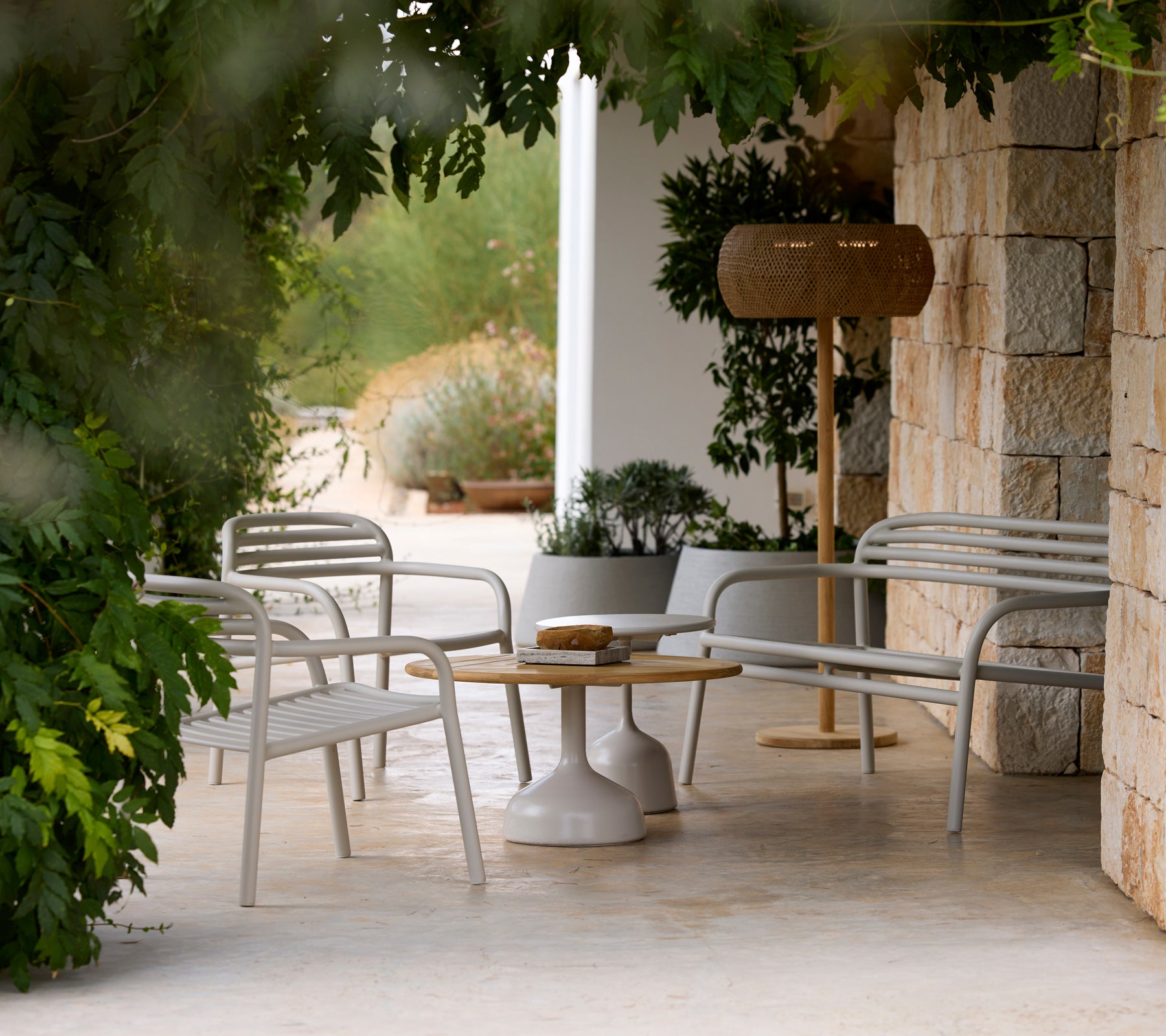 Modern grey lounge chairs and a white table beside a wooden lamp in a serene outdoor setting.