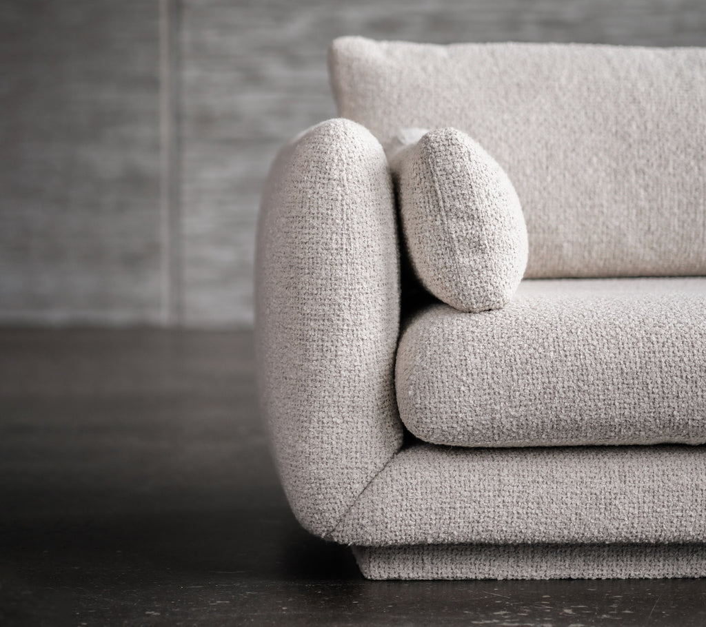 Modern light grey sofa with rounded arm and cushion detail.