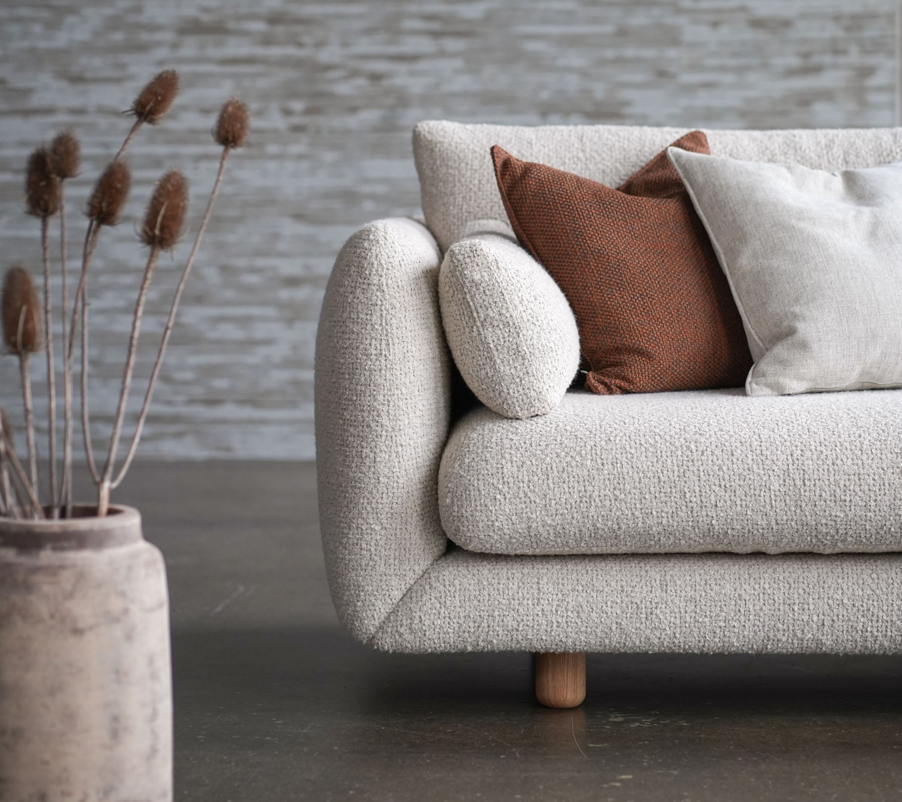 Cozy sofa with bloom upholstery, teak legs, and rise cushions, accompanied by decorative vase and dried flowers. Elegant and inviting design.