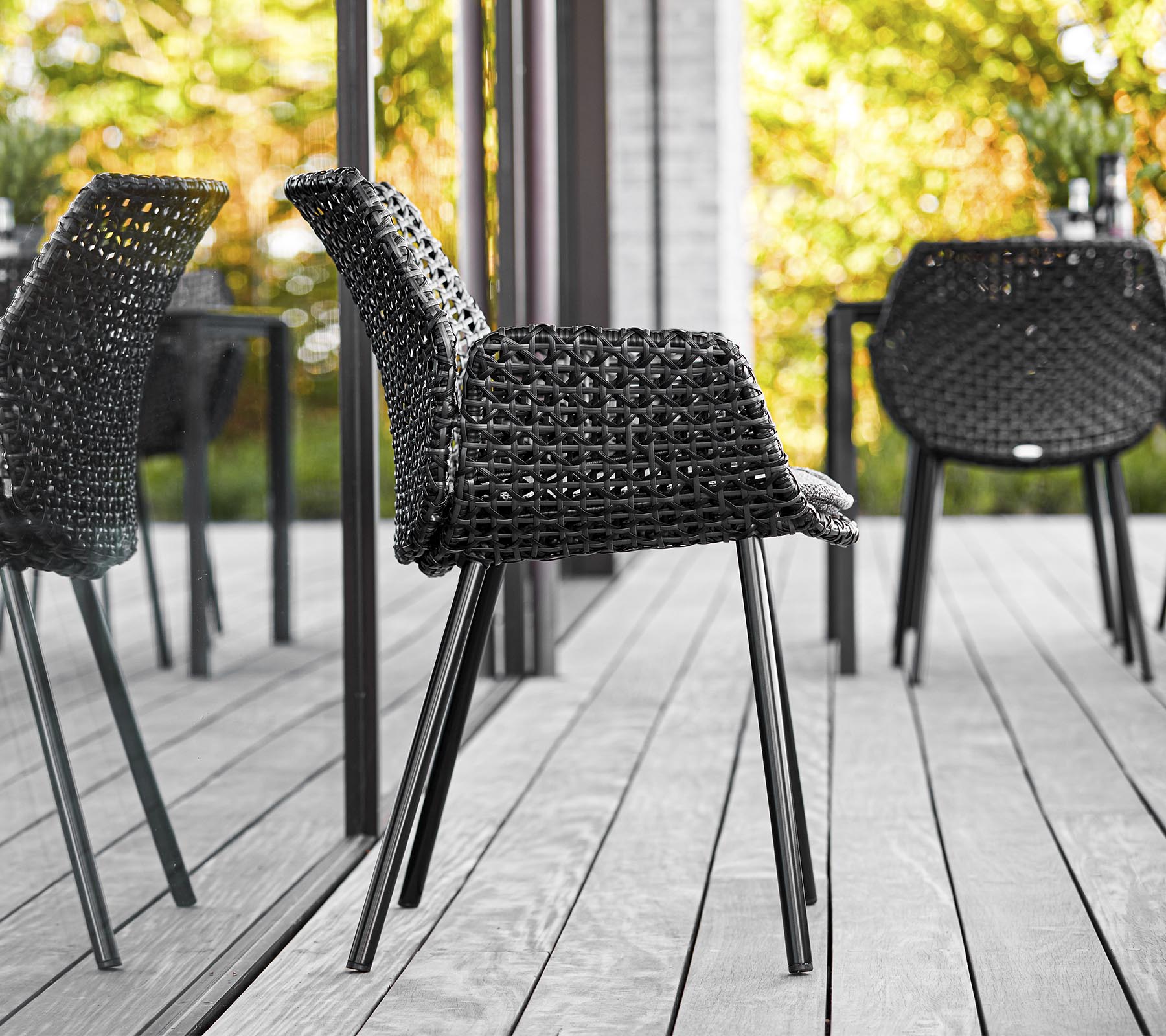 Stylish black woven chair with sleek legs, set against a backdrop of greenery and reflections, enhancing modern outdoor aesthetics.